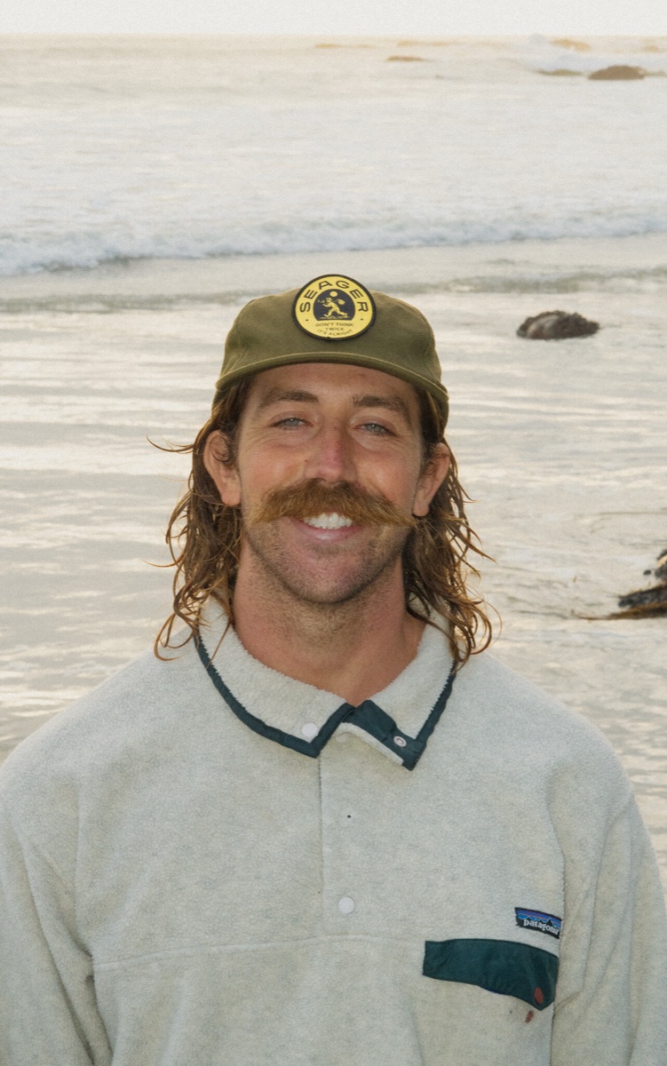 Justin DeMoss on the beach at Ocean Beach, smiling, ball cap on.